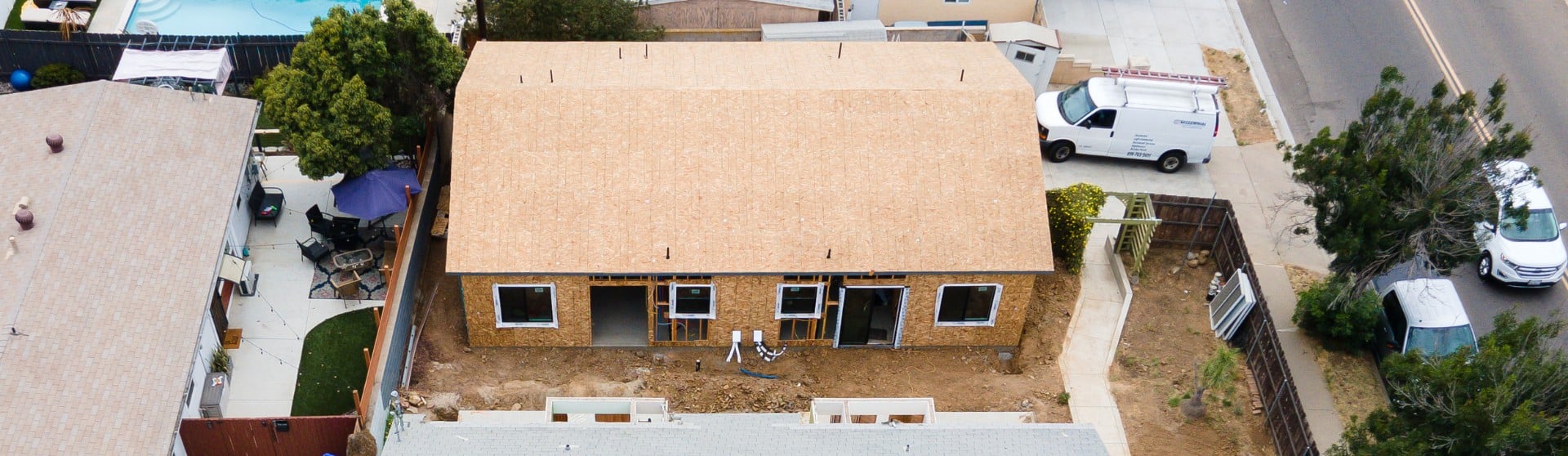 An aerial view of a house addition under construction. The image showcases the early stages of building, with the framework and roofing in place. Surrounding the construction site are existing homes and a neighborhood street, emphasizing the integration of new additions into established residential areas. This visual highlights the process and scale of adding significant new living spaces to a home.